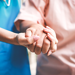 a carer in blue scrubs holding hands with an elderly person wearing a pink shirt. 
