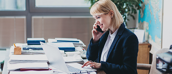 a lady in office on the phone, typing on a laptop while sorting files as part of administration duties