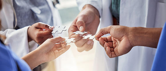 two doctors and two care workers each holding a puzzle piece to one another 